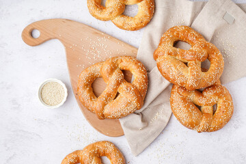 Wooden board with tasty pretzels and sesame seeds on light background