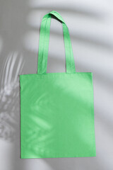 High angle view of green canvas bag with copy space and leaf shadow on grey background