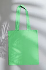 Gordijnen High angle view of green canvas bag with copy space and leaf shadow on grey background © vectorfusionart