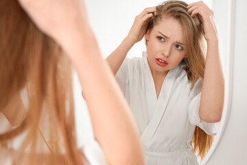 Fototapeta premium Worried young woman with hair loss problem looking in mirror at home