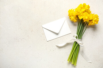 Beautiful narcissus flowers with ribbon and envelope on light background