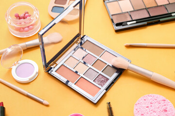 Decorative cosmetics with makeup brushes on yellow background, closeup