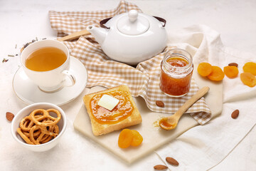 Tasty toast with apricot jam, cookies and cup of tea on light background