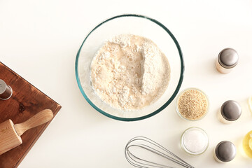 Bowl with flour and ingredients for preparing Italian Grissini on white background