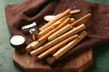 Wooden board with tasty Italian Grissini on green background