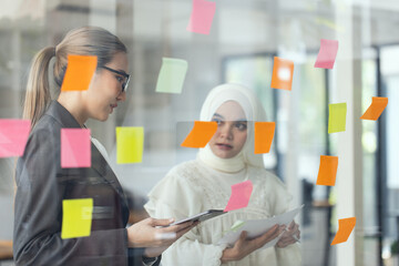 Asian woman team working on project plan using sticky papers notes on glass wall, people meeting to share idea, Business design planning concepts.