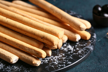 Slate board with tasty Italian Grissini on dark background, closeup