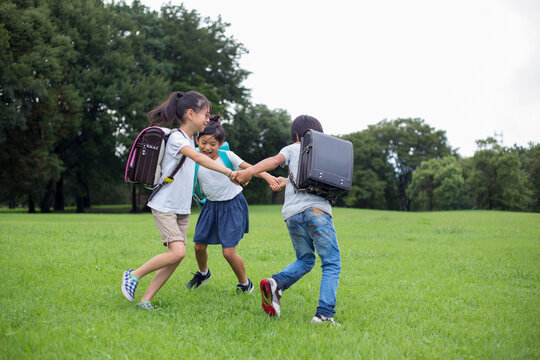 草原で手を繋いで遊ぶランドセルを背負った小学生達