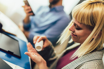 Woman sitting by the desk in the office and taking medical pills