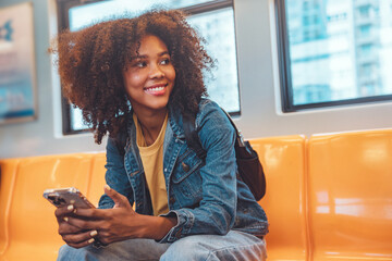 Happy young African American woman passenger smile and using smart mobile phone in subway train...