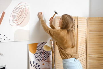 Young woman nailing on light wall at home