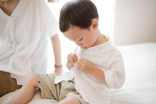 洋服のボタンをとめようとする男の子とそれを見守る母親