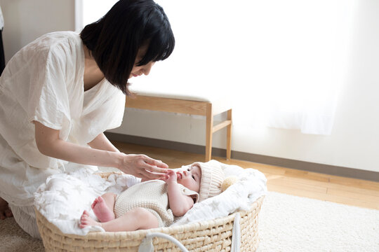 リビングルームのクーファンで寝ている赤ちゃんとあやす母親