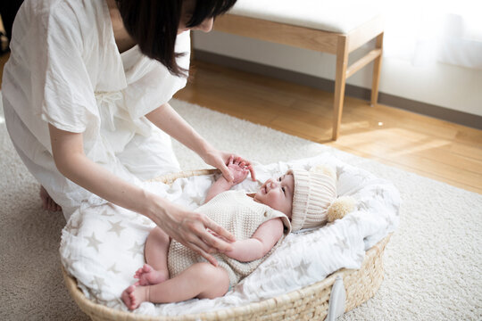 リビングルームのクーファンで寝ている赤ちゃんとあやす母親
