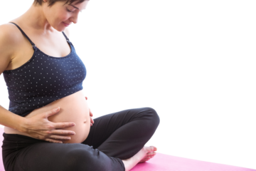 Happy pregnant woman holding belly while sitting on exercise mat