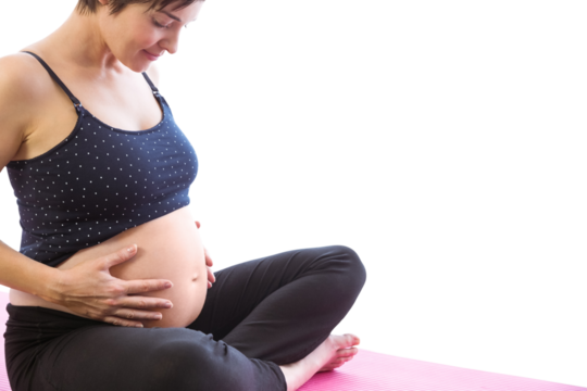 Happy pregnant woman holding belly while sitting on exercise mat