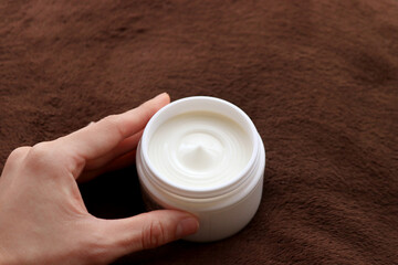 白い容器に入った保湿クリームを持つ手（美容イメージ）