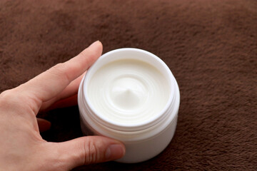 白い容器に入った保湿クリームを持つ手（保湿イメージ）