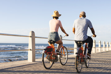 Diverse couple riding bikes along promenade by the sea