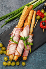 Board of tasty Italian Grissini with bacon on dark background