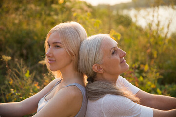 portrait of a smiling senior woman with gray hair and a adult daughter relaxed outdoors at sunset....
