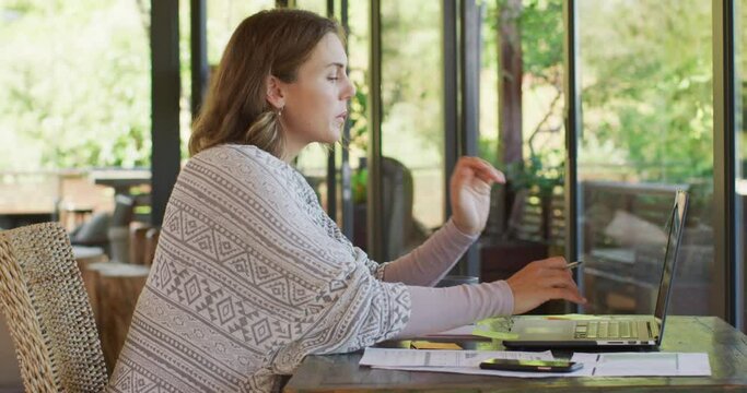 Caucasian pregnant woman sitting at desk, working remotely on laptop