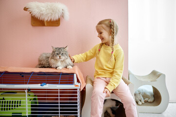 Happy smiling little girl child playing with cat indoors