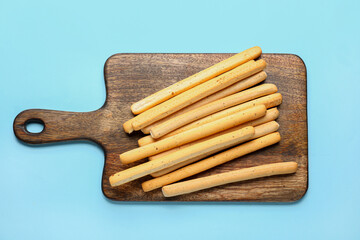 Wooden board with tasty Italian Grissini on blue background