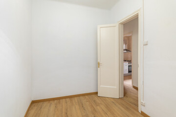 Empty white room with a front door and a view of a cozy kitchen with wooden laminate in a new apartment. Concept of preparation for furnishing and housewarming. Copyspace