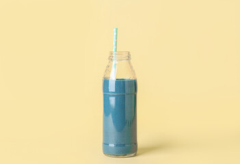 Glass bottle of tasty blue smoothie with straw on yellow background