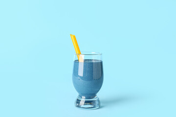 Glass of tasty blue smoothie with straw on color background
