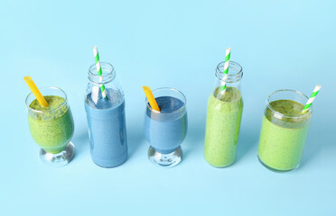 Glasses and bottles of different tasty smoothie with straws on blue background