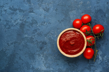 Bowl with tasty tomato paste and fresh vegetables on blue grunge background