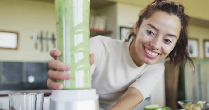 Happy biracial woman using blender, preparing smoothie in kitchen