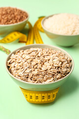 Bowls with oatmeal flakes and yellow measuring tape on green background. Diet concept