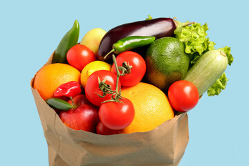 Paper bag with vegetables and fruits on light blue background