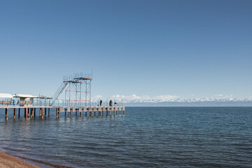 Sunny Pier on Lake with Snowy Mountains in the Distance