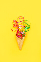 Composition with ice cream cone and confetti on yellow background