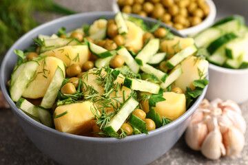 Bowl of tasty Potato Salad with vegetables on grunge background, closeup