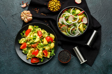 Bowl and plate of tasty Potato Salad with vegetables on dark background
