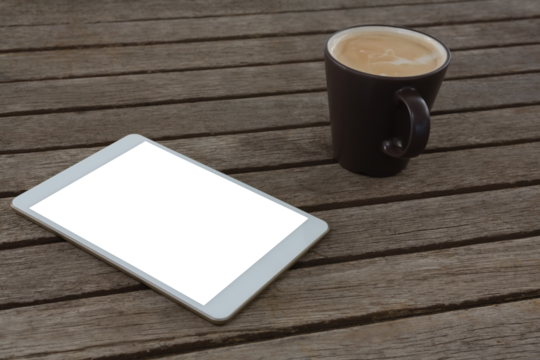 Digital tablet and cup of coffee on wooden plank