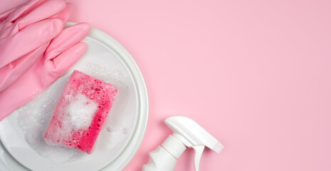 Detergent, soapy kitchen sponge and clean plates on a pink background. Close-up. Copy space. Top view. Selective focus.