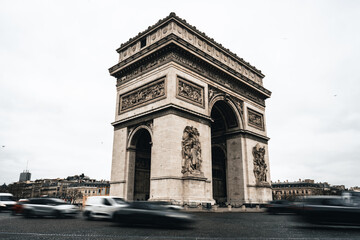 Fototapeta na wymiar Arc de Triomphe mit Autos im Vordergrund welche in Bewegung sind und hellem bewölkten Himmel