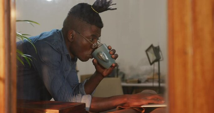 Thoughtful african american craftsman wearing glasses drinking coffee in leather workshop