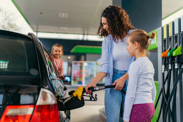 the mother fills the car with fuel at the gas station and talks to her daughters about the upcoming...