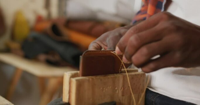 Hands of african american craftsman preparing wallet in leather workshop