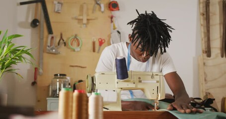 Focused african american craftsman with dreadlocks using sewing machine in leather workshop