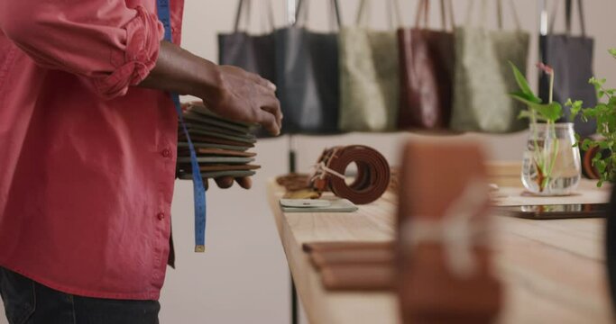 Hands of african american craftsman arranging wallets on wooden surface in leather workshop