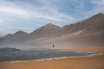 Stunning view a person walking on the Cofete beach surrounded by the chain of mountains of the Jandía Natural Park. Fuerteventura, Canary Islands.