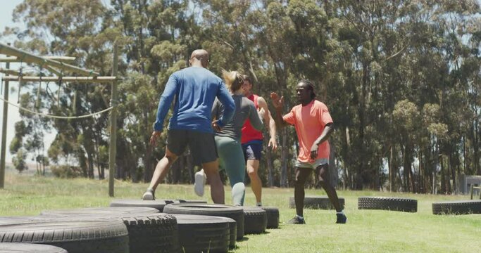 Diverse fit group running through tyres and high fiving in the sun at obstacle course